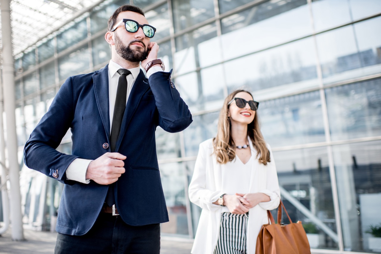 A discrete security professional in a suit walks alongside a smiling, well-dressed businesswoman.